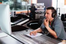 Hiring Voice Actors Producer sitting at audio board looking at computer screen to hire voice actor