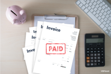What To Include in a Voice Over Invoice An invoice marked paid on a desk with a piggy bank and calculator