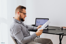 A producer listening to voice over audio on a laptop while reviewing a script